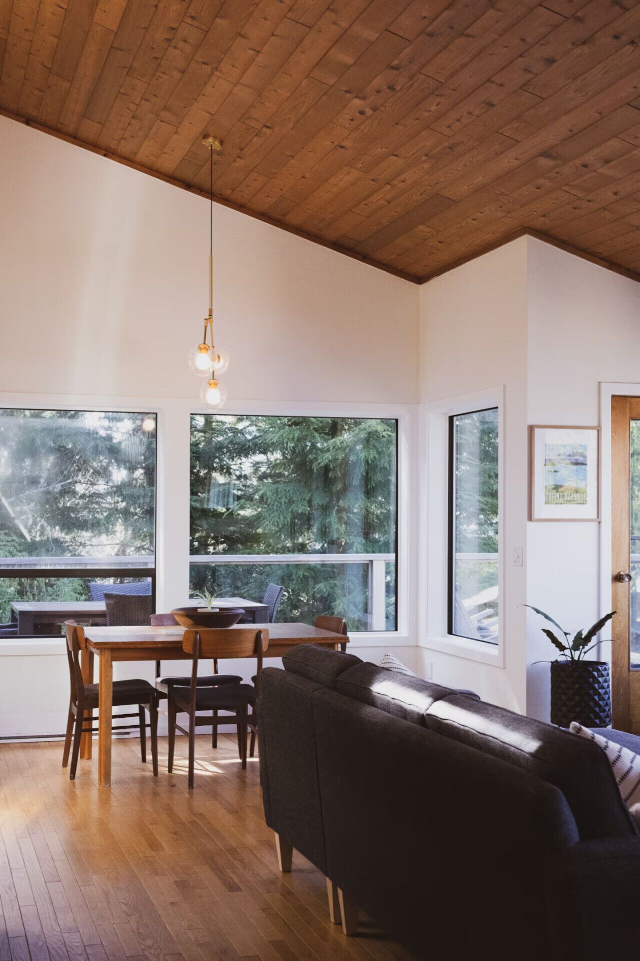 A modern interior with a wooden ceiling, large windows, a dining table, and a sofa.