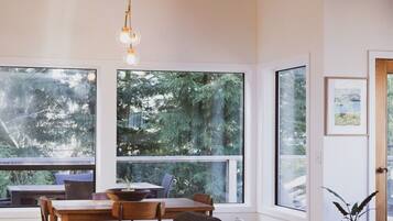 A modern interior with a wooden ceiling, large windows, a dining table, and a sofa.