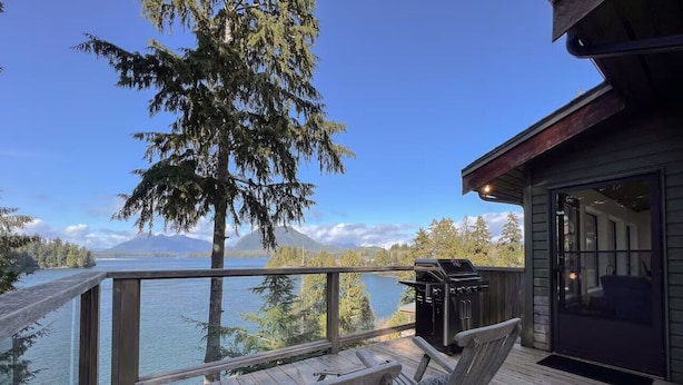 A wooden deck with a view of a lake and mountains, a grill, and a glass door leading to an interior space. - Marielle’s Lookout -  Your Oceanfront Escape (Tofino)