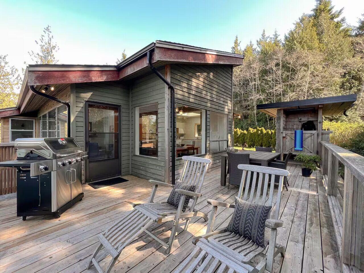 A deck with a grill, chairs, and a small building with a door and windows.