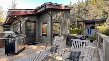A deck with a grill, chairs, and a small building with a door and windows.