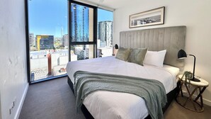 Un dormitorio moderno con una cama grande, un ventilador de techo y vistas a la ciudad a través de ventanales de gran altura.