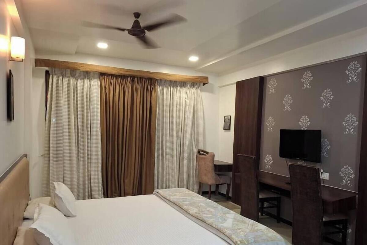 Quarto de hotel com cama, escrivaninha, cadeira, televisão e ventoinha no teto.