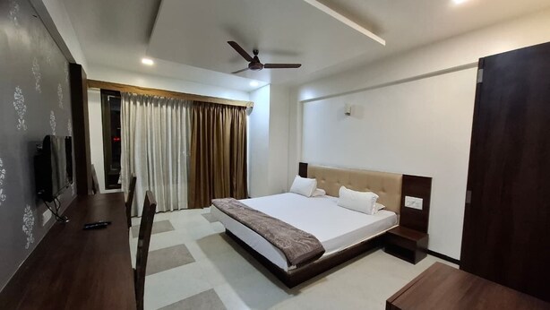Une chambre d’hôtel avec un grand lit, un bureau avec une chaise, un ventilateur de plafond et une fenêtre avec des rideaux.