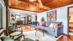 Ein großzügiger Wohnbereich mit grauem Sofa, grünen Sesseln und einer Holzbalkendecke.