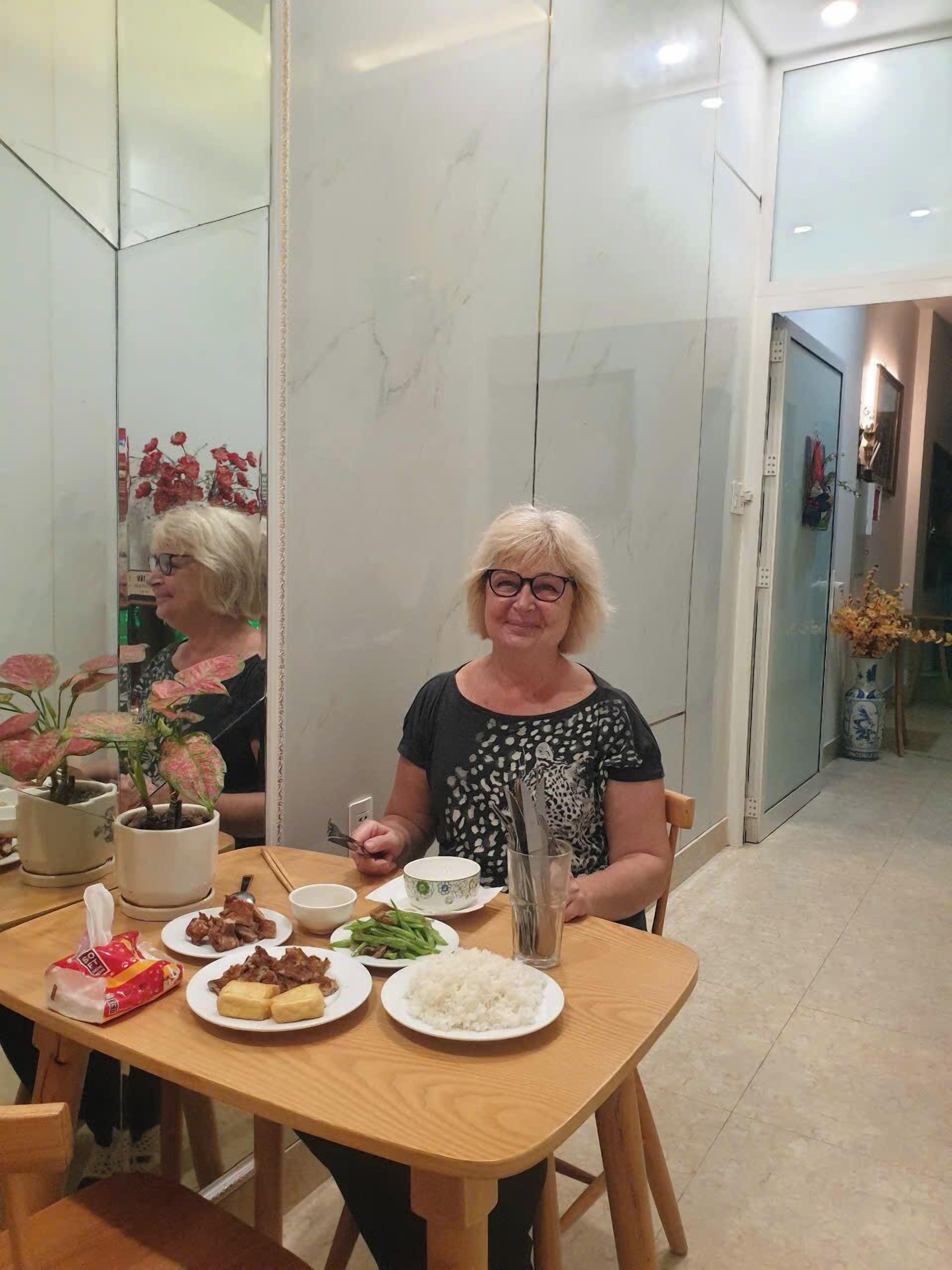 A dining area with a table set for two, featuring plates of food, a cup, and a vase with flowers.
