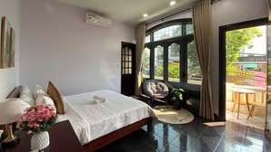 A modern hotel room with a large bed, a sitting area with a chair and a small table, and a view of the outdoors through a large window. - Lavande Hue Homestay (Hue)