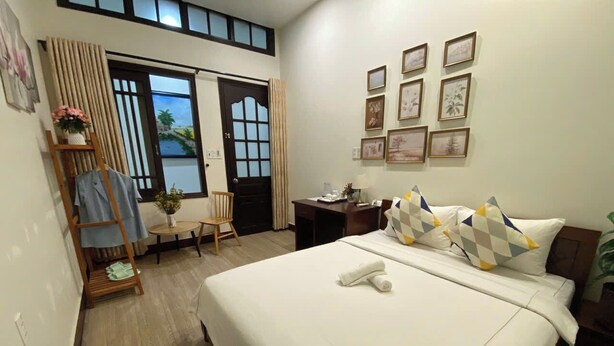 A hotel room with a large bed, a desk, a chair, and a window with curtains. - Lavande Hue Homestay (Hue)