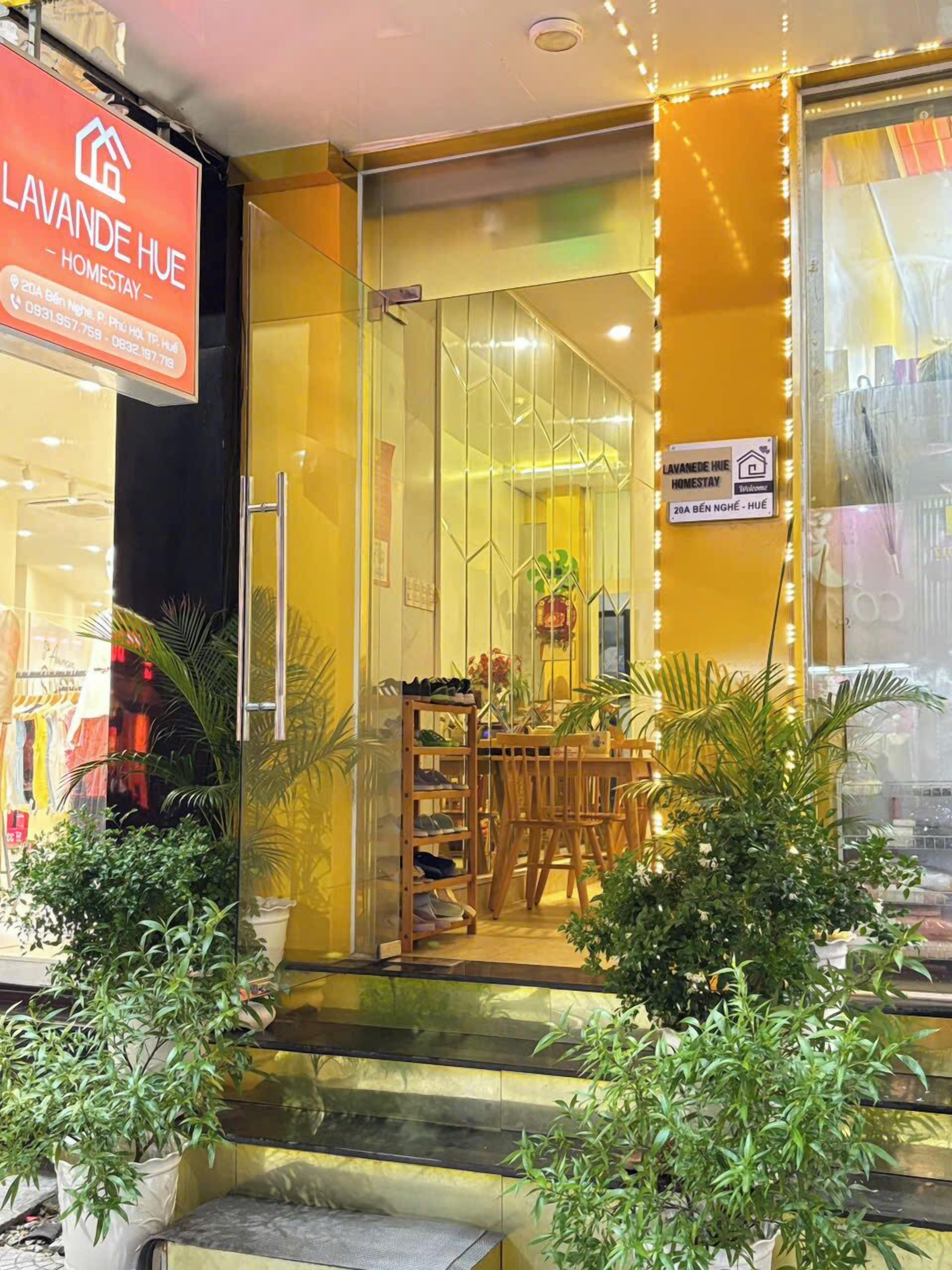 L’entrée d’un hôtel, avec une porte en verre, un porte-chaussures à l’extérieur et une enseigne indiquant « Lavande Hue Homestay ».
