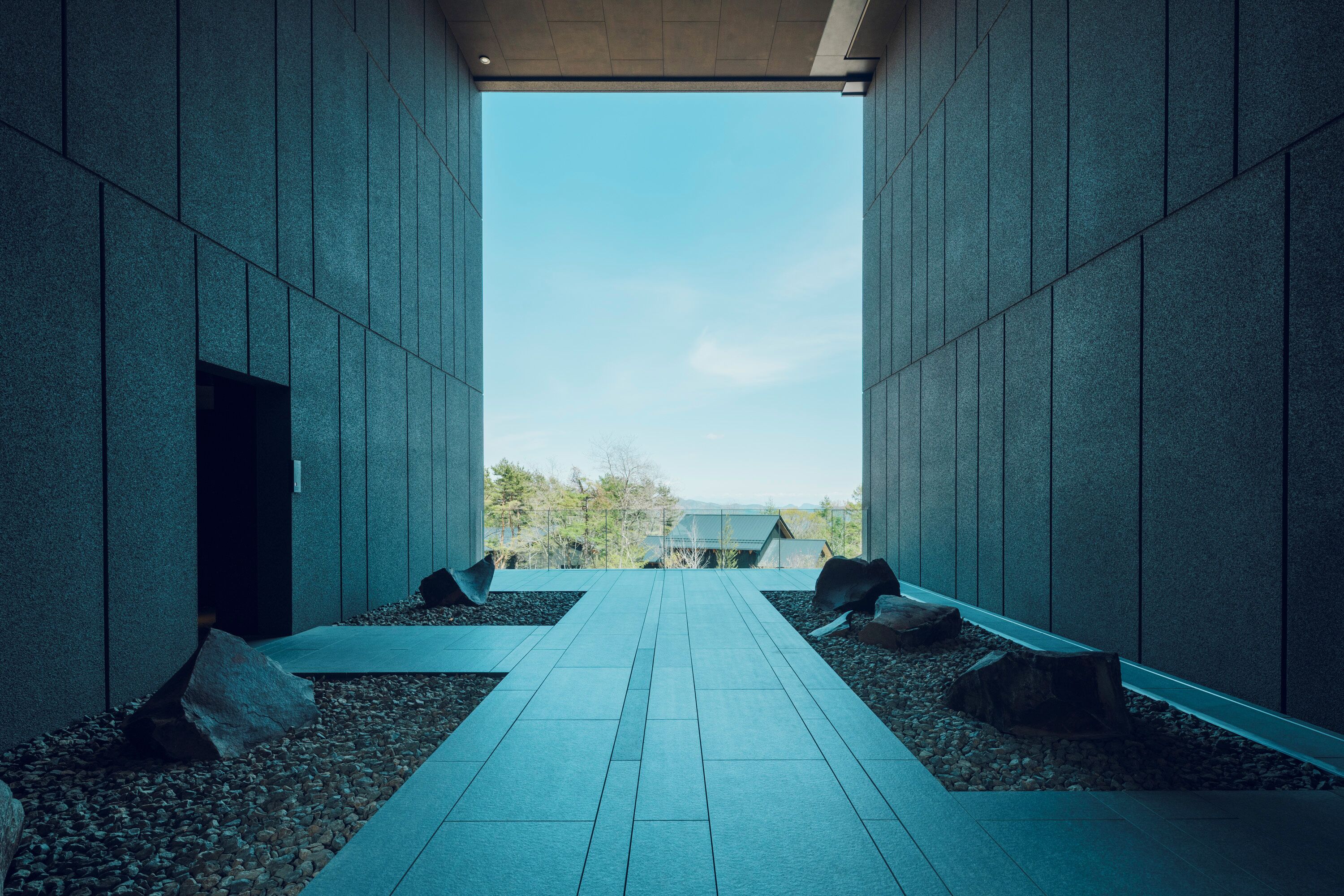 A corridor with a tiled floor leading to a glass door, flanked by walls with a textured surface.