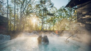 A hot spring with steam rising, surrounded by trees and a wooden structure. - Hoshino Resorts KAI Kusatsu (Kusatsu)