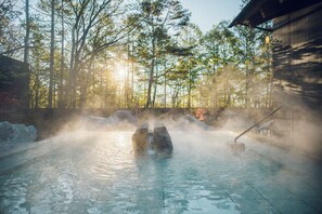 A hot spring with steam rising, surrounded by trees and a wooden structure. - Hoshino Resorts KAI Kusatsu (Kusatsu)