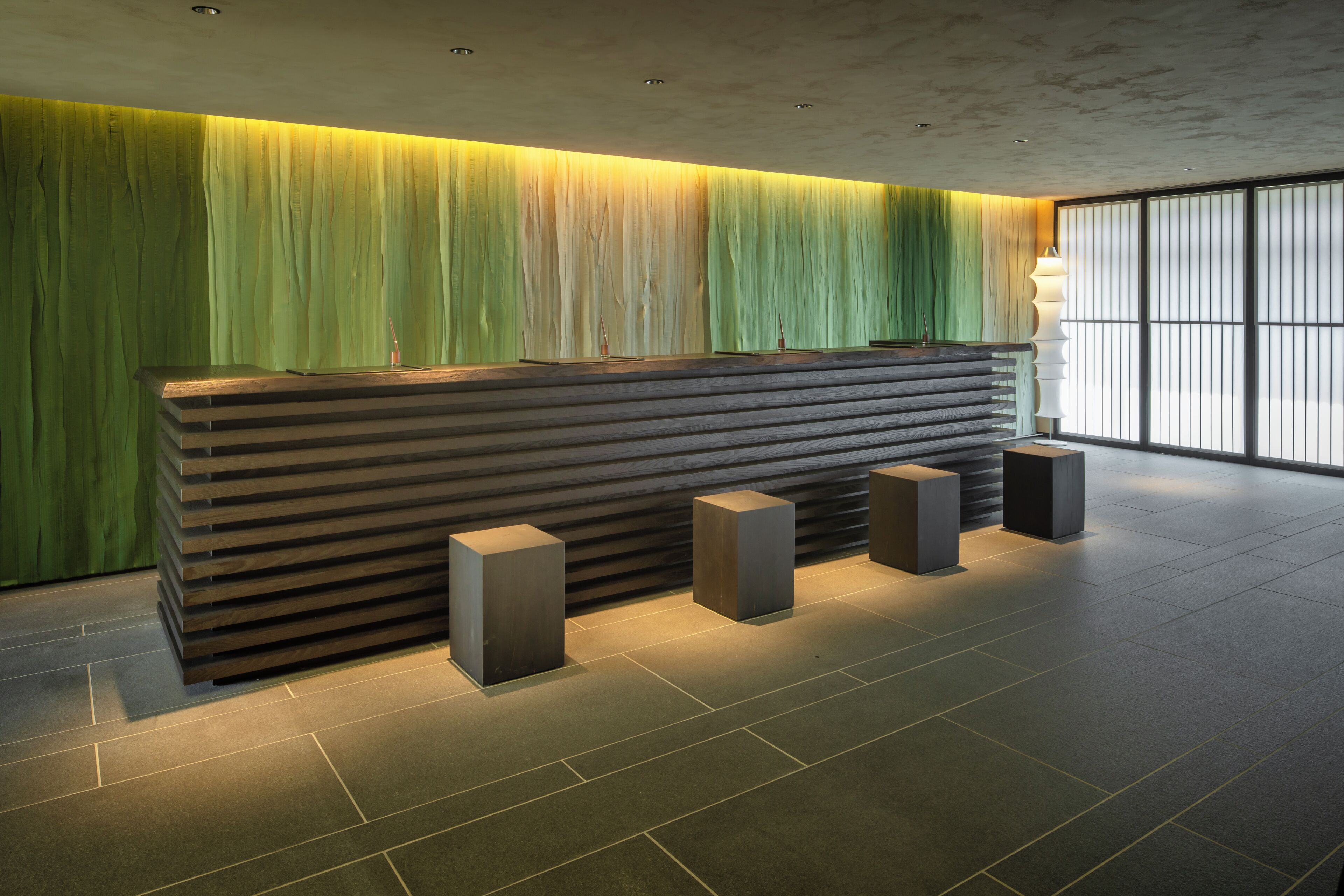 A reception desk with a modern design, flanked by vertical blinds and a large window.