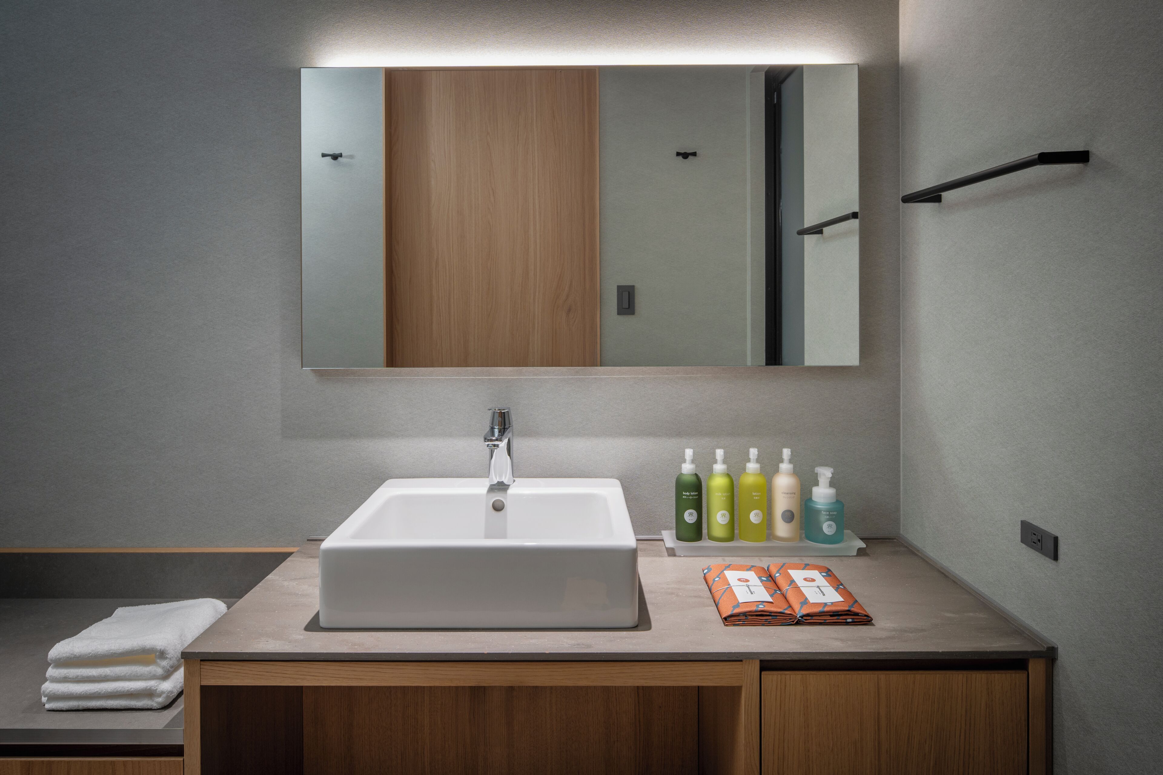 A modern bathroom with a large mirror, a sink, and a shelf with toiletries.