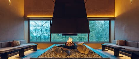 Un interior moderno con una chimenea central, zonas de estar y ventanas amplias.
