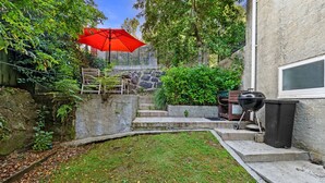 Ein Garten mit einem roten Sonnenschirm, einem Grill und einer Steinmauer.