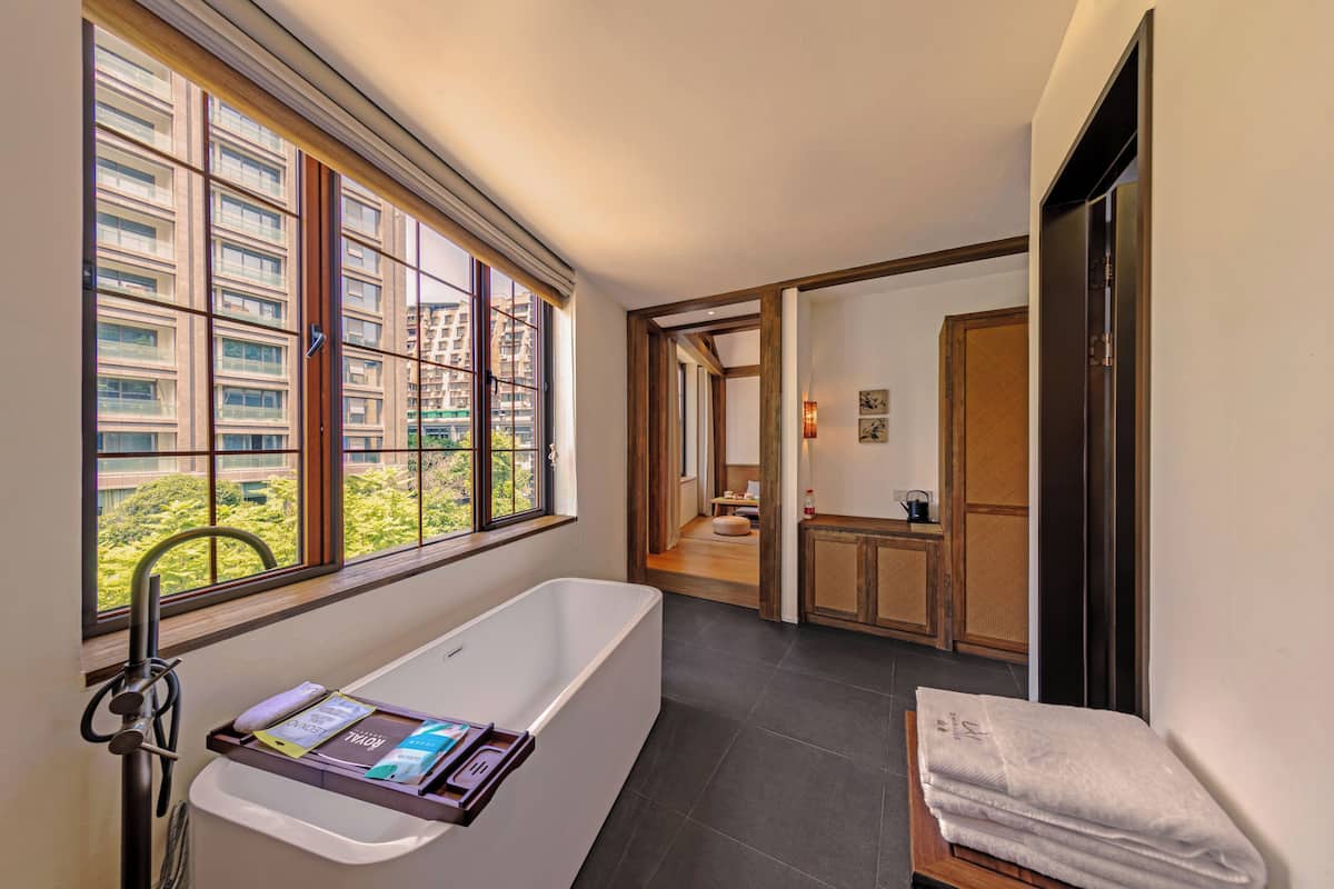 A modern bathroom with a bathtub, a window with a view of buildings, and a wooden bench with towels.