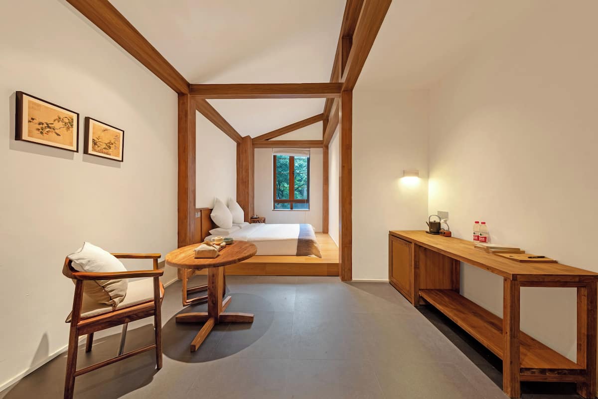 A bedroom with a loft bed, a wooden desk, a chair, and two framed artworks on the wall.