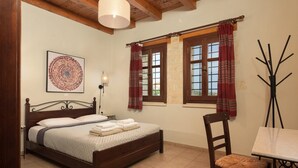 Ein Schlafzimmer mit einem hölzernen Bett, einem Nachttisch, einem Sessel, einem Fenster mit Vorhängen und einer Wandlampe.