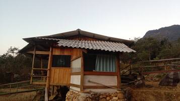 A wooden cabin with a tiled roof, a window with curtains, and a stone base.