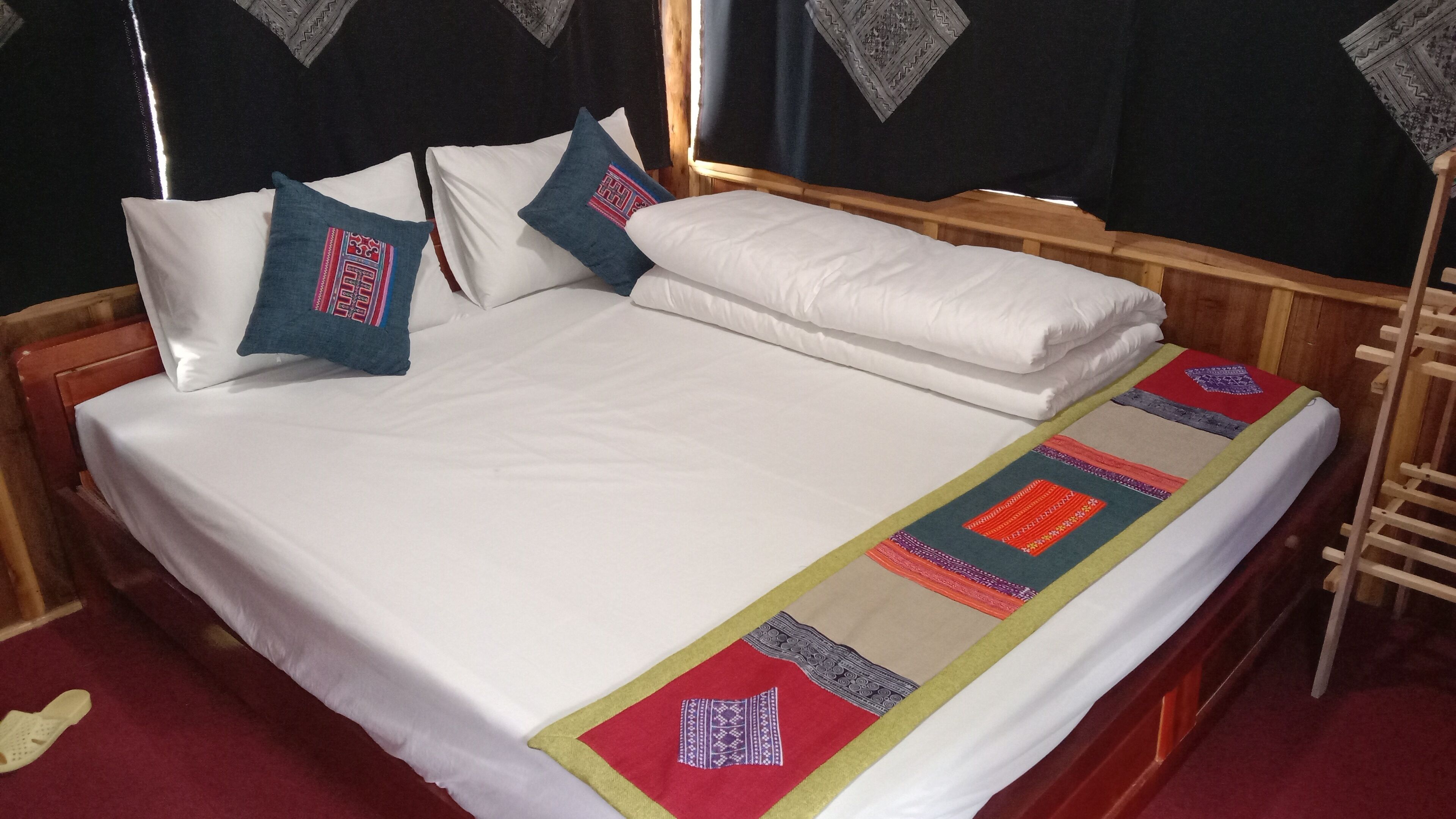 A neatly made bed with white linens and a colorful blanket, two pillows with embroidered designs, and a wooden headboard.