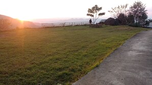 A grassy field with a concrete path, a metal railing, and a small building in the background. - To Ech Homestay (Sin Suoi Ho)