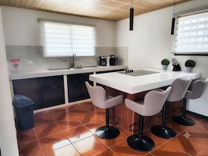 Una cocina moderna con encimera blanca, taburetes negros y una ventana con persianas.