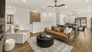 Een moderne woonkamer met een bank, fauteuils, een salontafel en een eethoek, met een keuken op de achtergrond.