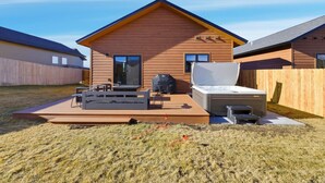 Een gelijkvloers houten huis met een terras, inclusief een bank, een tafel en een barbecue.
