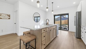 Een moderne keuken met een centraal eiland, hanglampen en uitzicht op de omgeving.