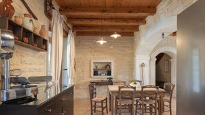 A rustic kitchen with stone walls, wooden beams, and a dining area with wooden chairs and a table. - Villa Dione, 3 BDR, Forest Views, Private Pool, Furnished Terrace, Crete (Rethymno)