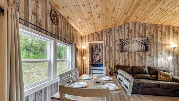 A wooden interior with a dining table set for four, a sofa, and a painting on the wall.