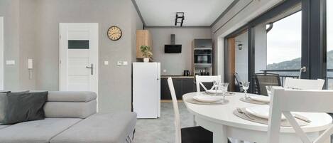 A modern living space with a sofa, dining table, chairs, a kitchen area, and large windows.