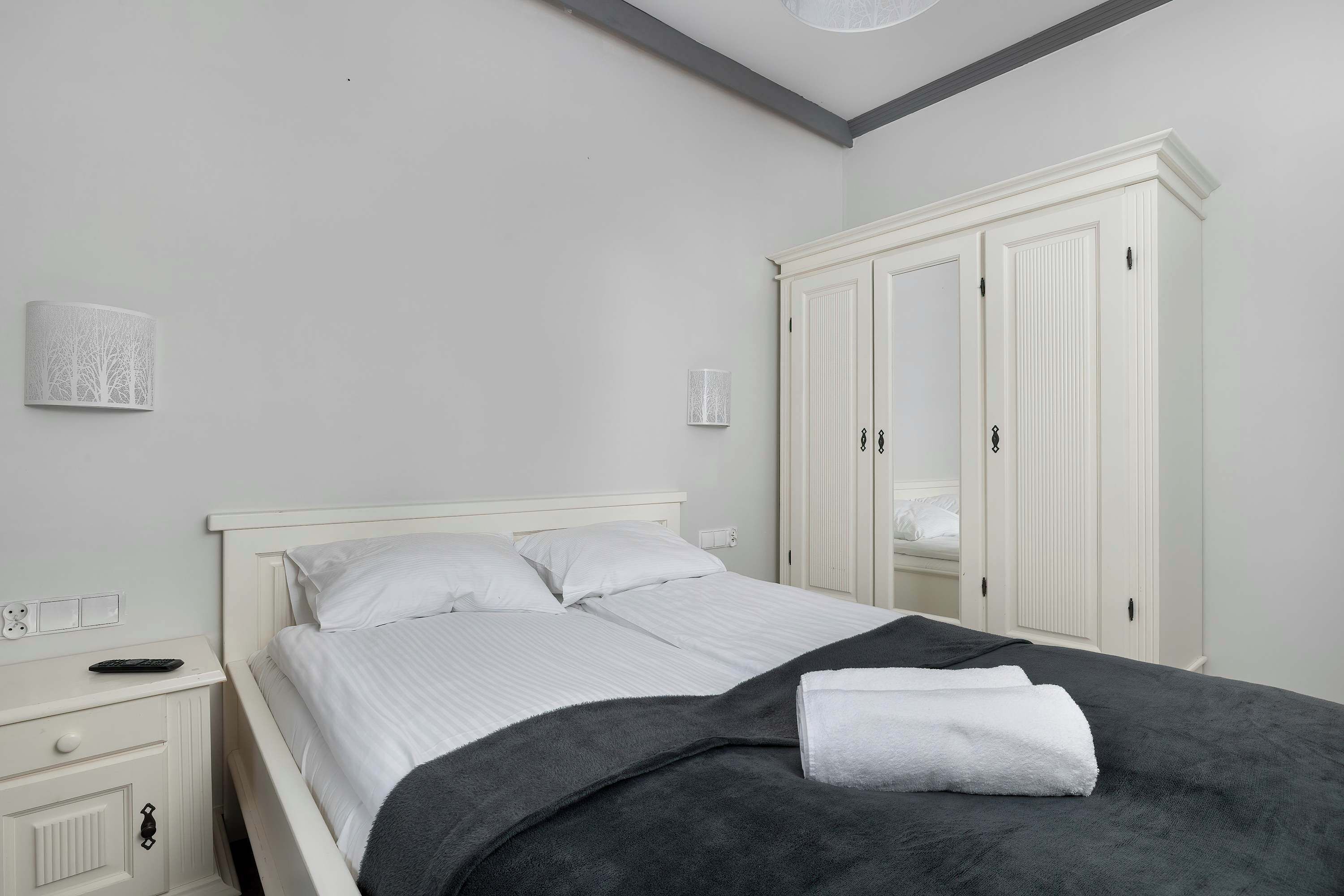 A bedroom with a bed, white wardrobe, bedside table, and wall-mounted lamp.