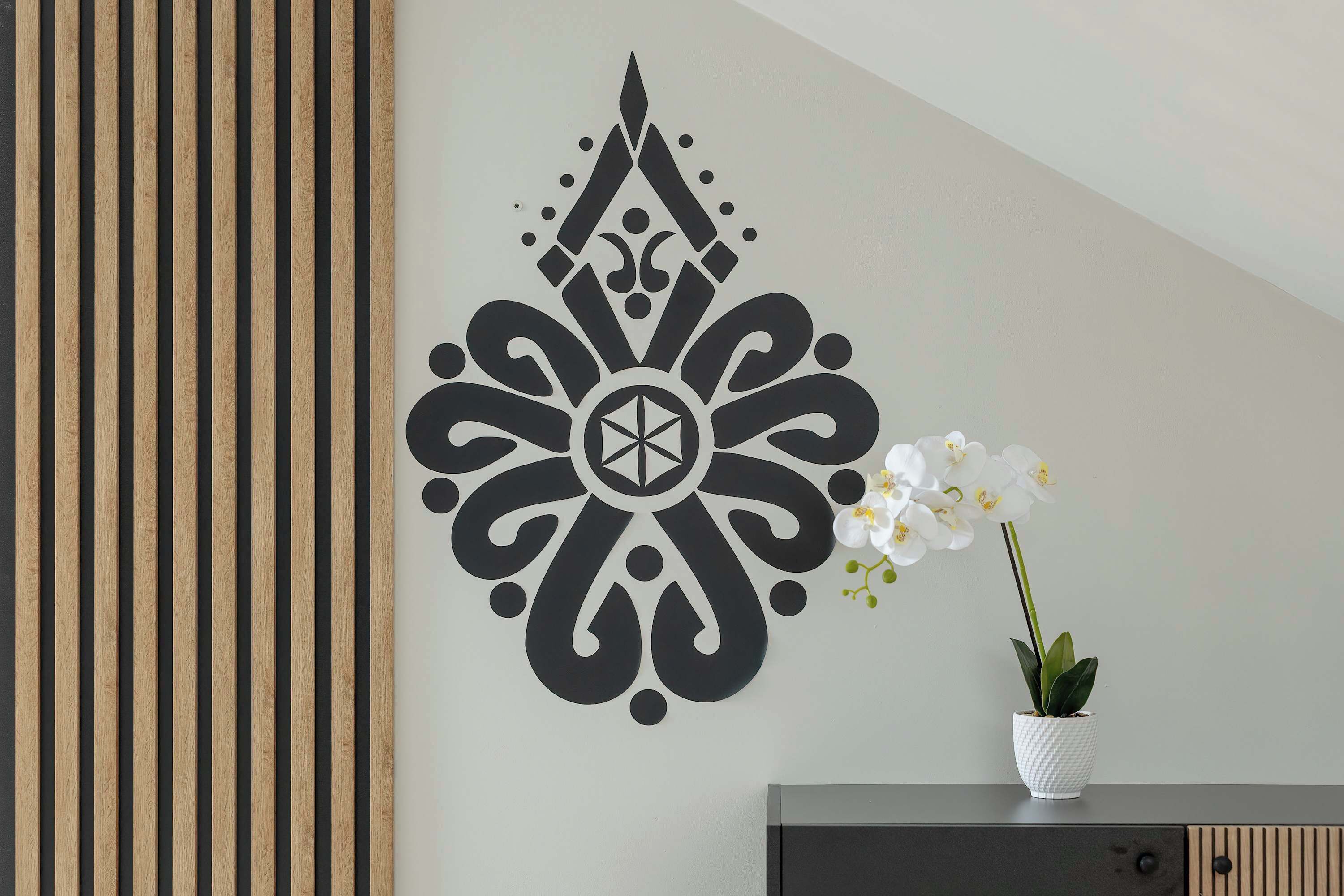 A wall with a geometric pattern, a potted plant, and a dark-colored cabinet.