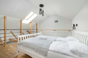 A bedroom with a sloped ceiling, a skylight, a bed with white bedding, a wooden headboard, and a wall-mounted light fixture.