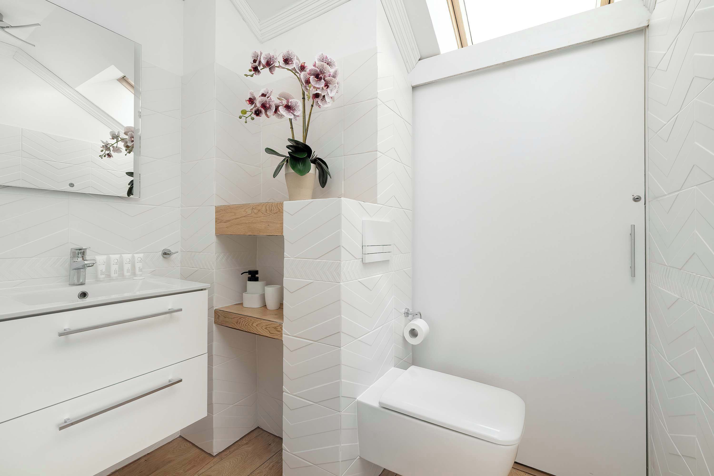 A modern bathroom with a white sink, mirror, toilet, and shower.