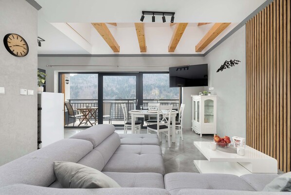 A modern living room with a sofa, a dining area, a TV, and a view of the outdoors.