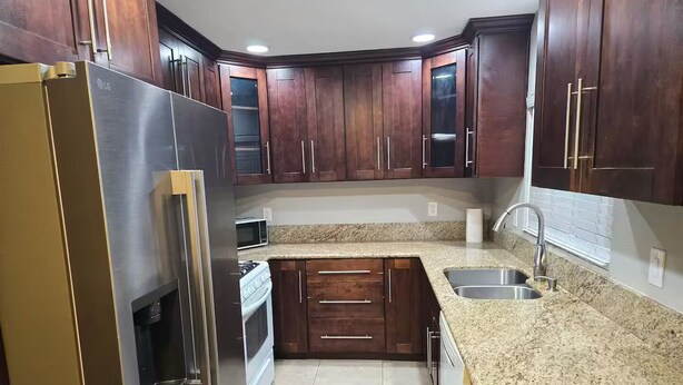 A kitchen with dark wooden cabinets, a stainless steel refrigerator, a granite countertop, and a built-in oven. - Spacious 3-Bed Home w/ Bonus Room in Loma Linda CA (Loma Linda)