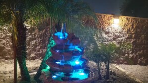 A multi-tiered water fountain with blue lighting, surrounded by palm trees and a stone wall. - Spacious 3-Bed Home w/ Bonus Room in Loma Linda CA (Loma Linda)
