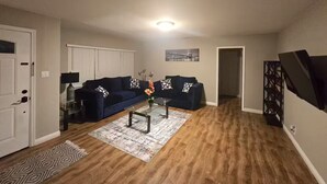A living room with a dark blue sofa, a glass coffee table, and a patterned rug. - Spacious 3-Bed Home w/ Bonus Room in Loma Linda CA (Loma Linda)
