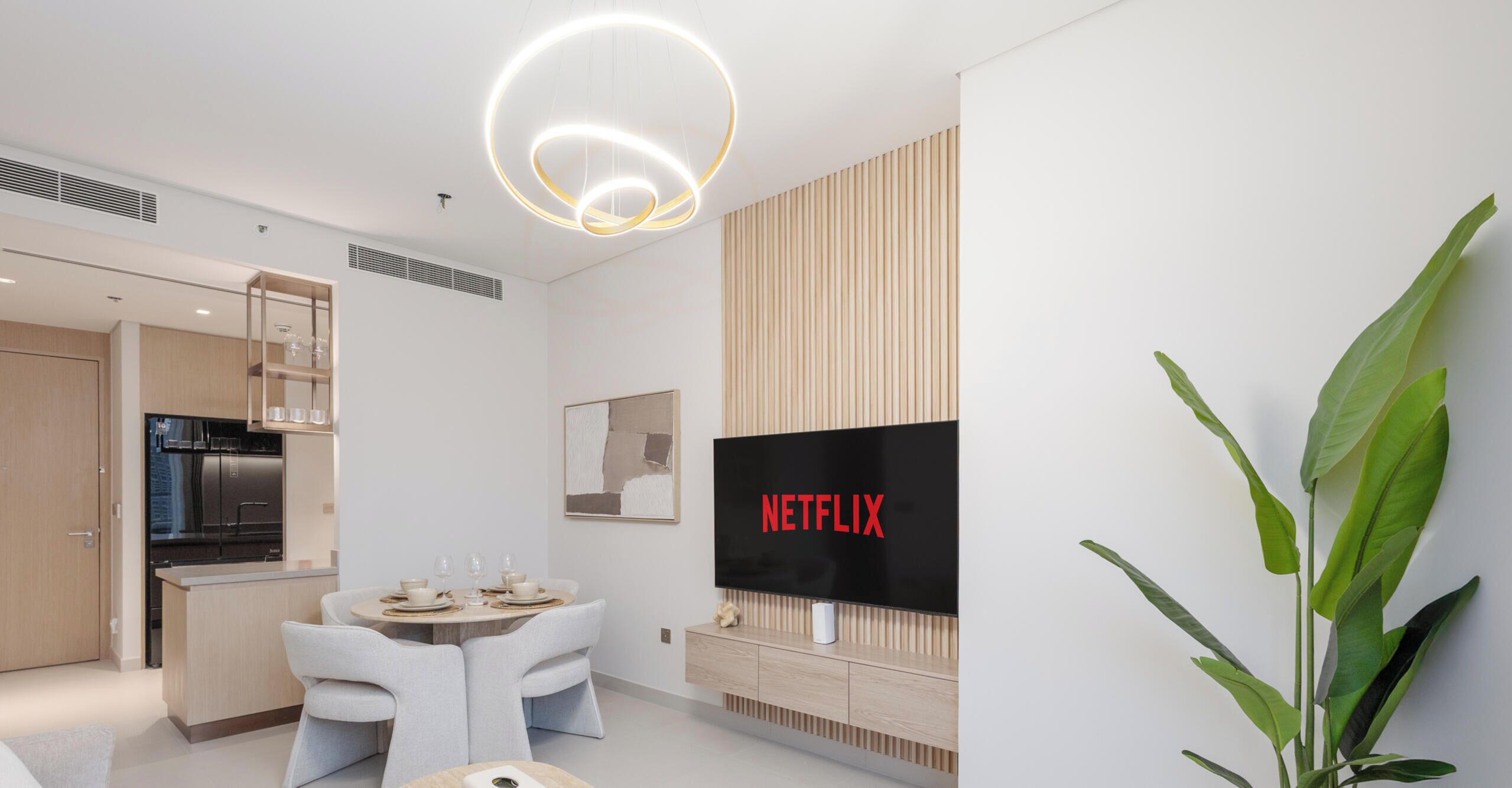 A modern living room with a dining area, a kitchen, and a TV displaying 'NETFLIX'.
