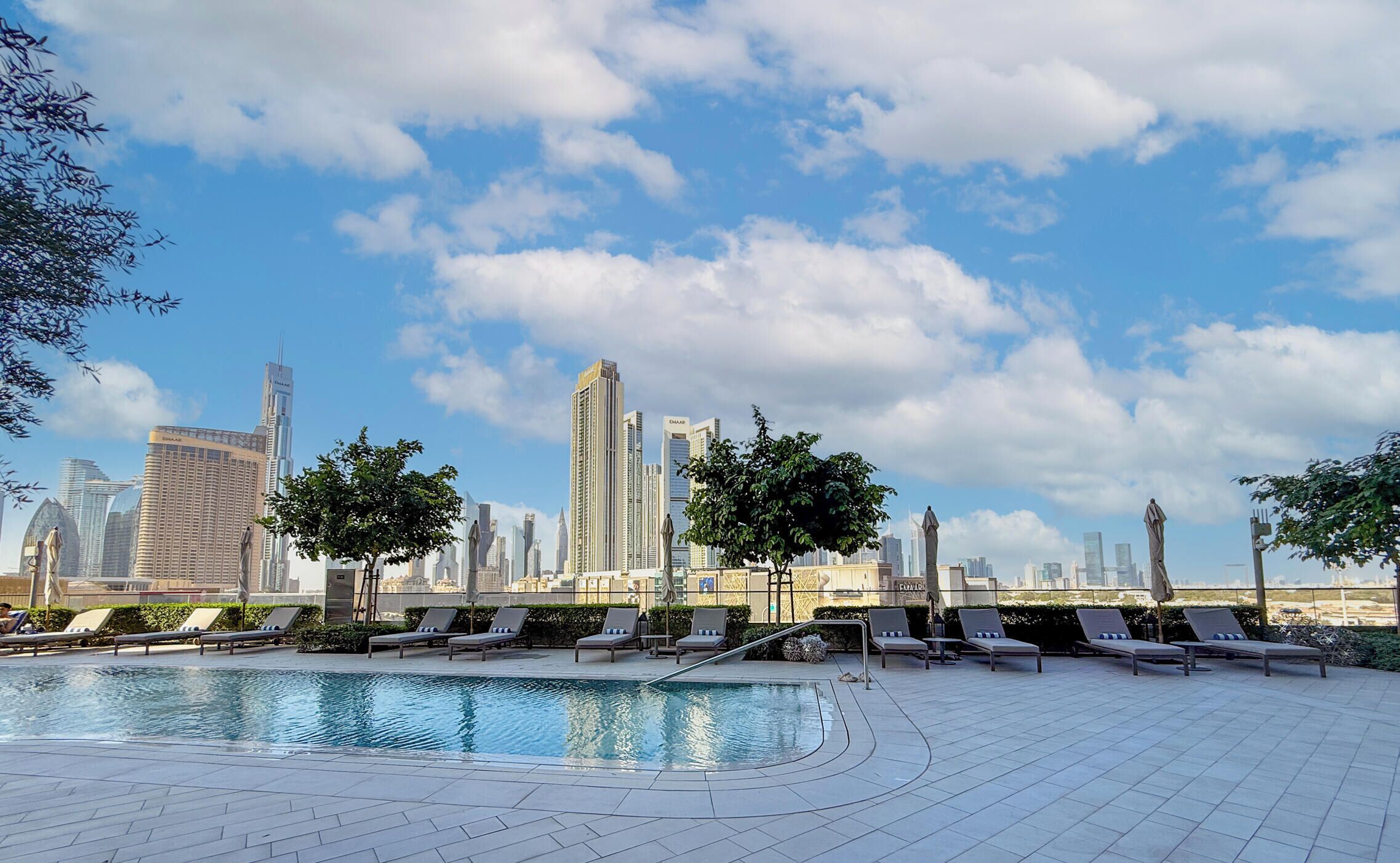 Un área de piscina en la azotea con sillones de descanso y un horizonte urbano al fondo.