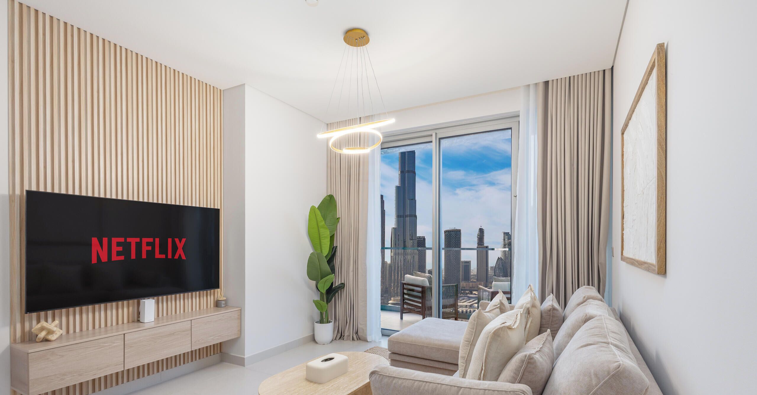 Ein modernes Wohnzimmer mit einem großen Flachbildfernseher, einem bequemen Sofa, einem Couchtisch und Blick auf eine Stadtlandschaft durch große Fenster.