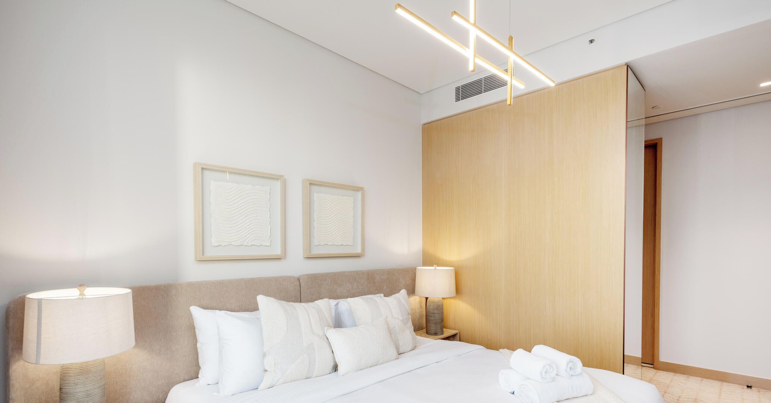 Ein modernes Hotelzimmer mit einem Bett, zwei Nachttischlampen, einem Holzschrank und zwei gerahmten Kunstwerken an der Wand.