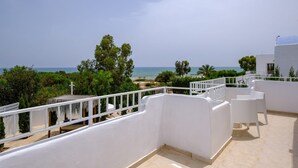 Terraço no telhado com vista para o mar, paredes brancas e um pequeno jardim.