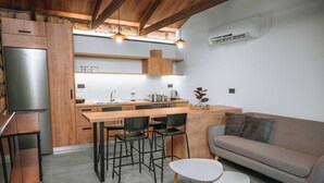 A compact kitchen with a built-in refrigerator, wooden cabinets, a dining area with chairs, a sofa, and a small table. - Villa Hydraea, Garden Views, 2 BDR, Ptivate Pool, Furnished Terrace, Soroni (Rhodes)