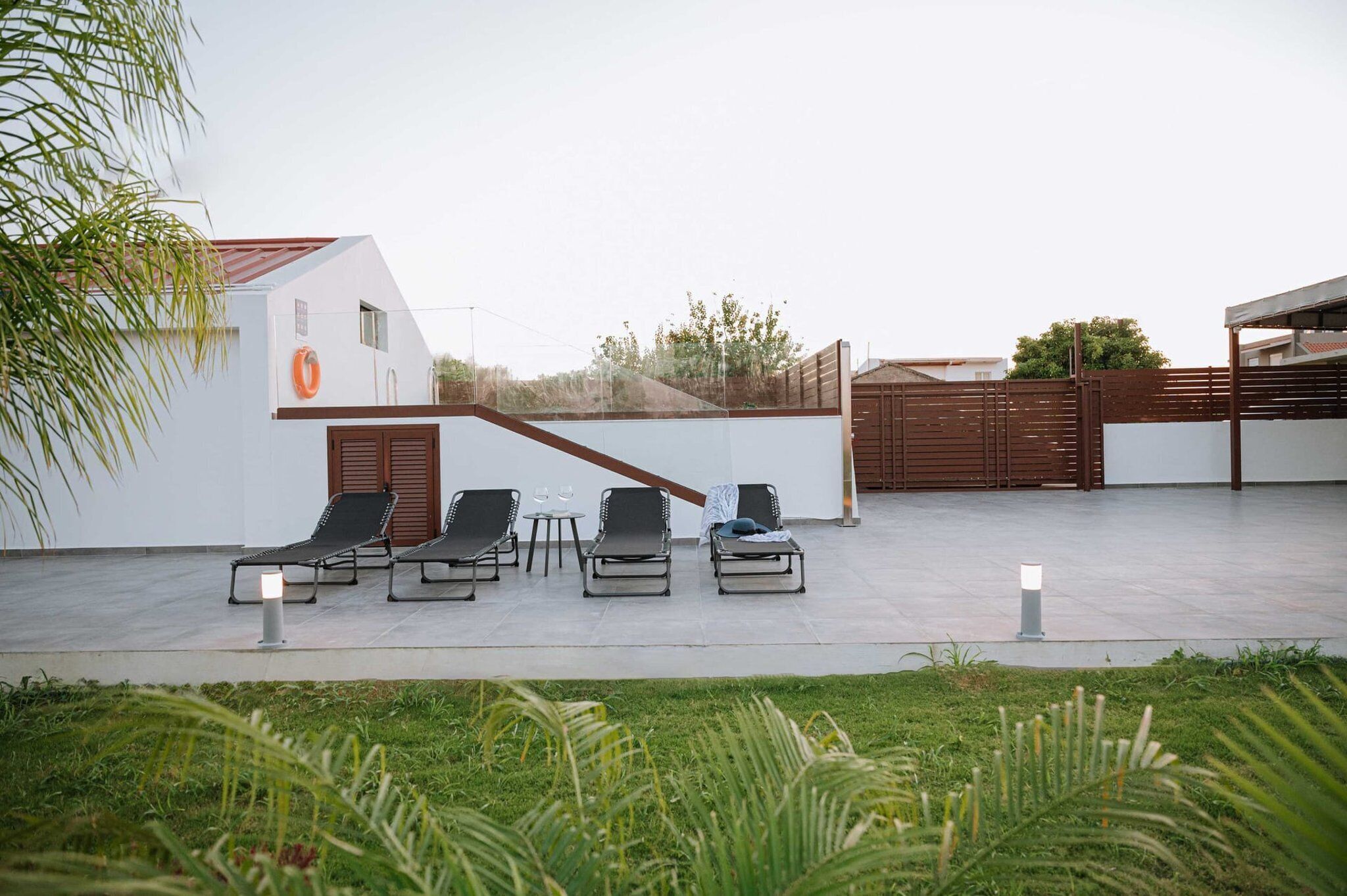 Un área de descanso al aire libre, moderna, con cuatro sillones y una pequeña mesa, rodeada por un edificio blanco con techo rojo.