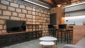 A modern kitchen with a stone wall, a flat-screen TV, and a bar area with stools. - Villa Hydraea, Garden Views, 2 BDR, Ptivate Pool, Furnished Terrace, Soroni (Rhodes)