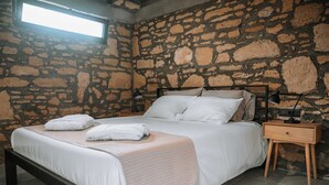 A bedroom with a stone wall, a bed with white linens, a bedside table with a lamp, and a window providing natural light. - Villa Hydraea, Garden Views, 2 BDR, Ptivate Pool, Furnished Terrace, Soroni (Rhodes)